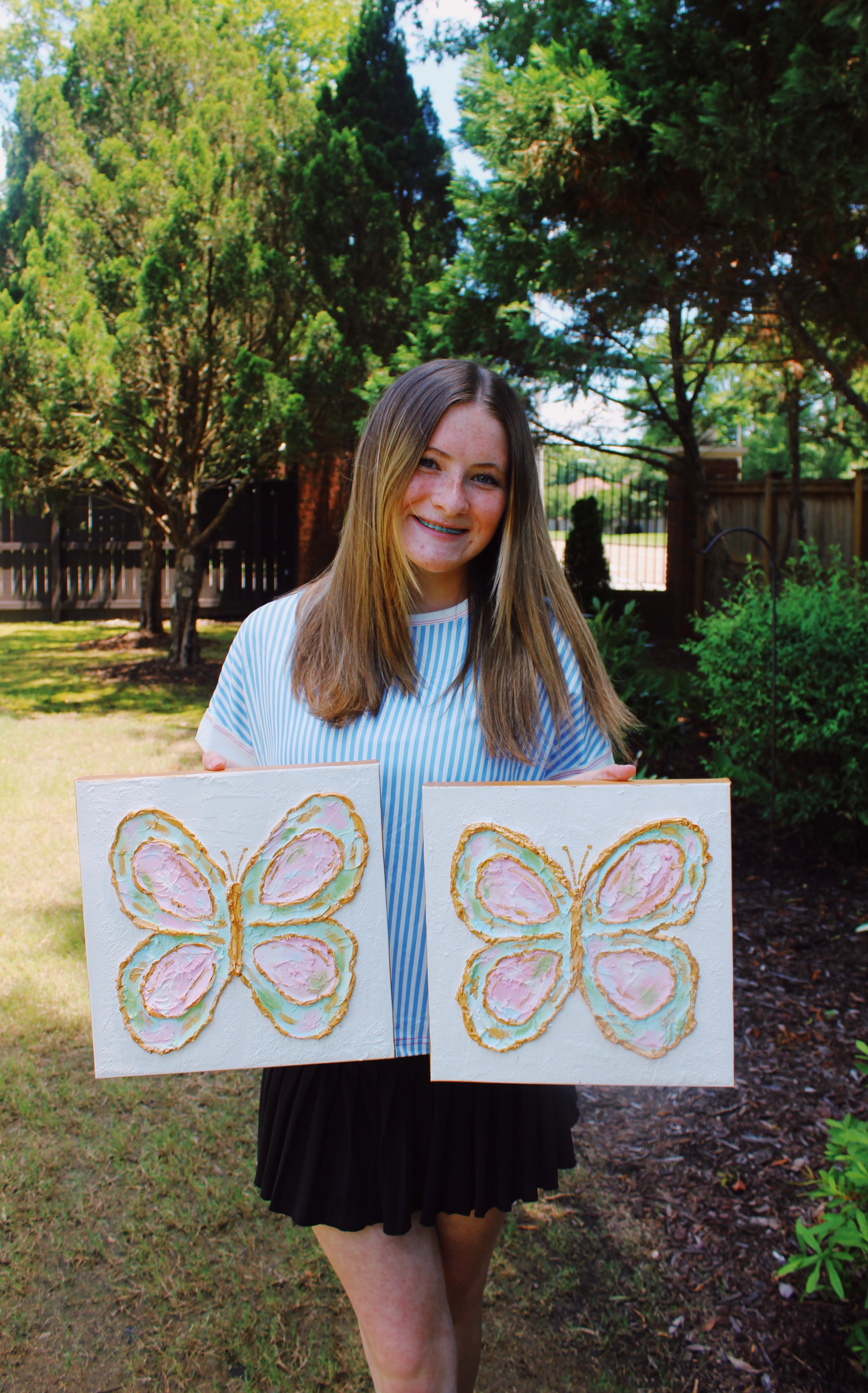 Katherine Nichols holding two hand-painted butterfly canvases